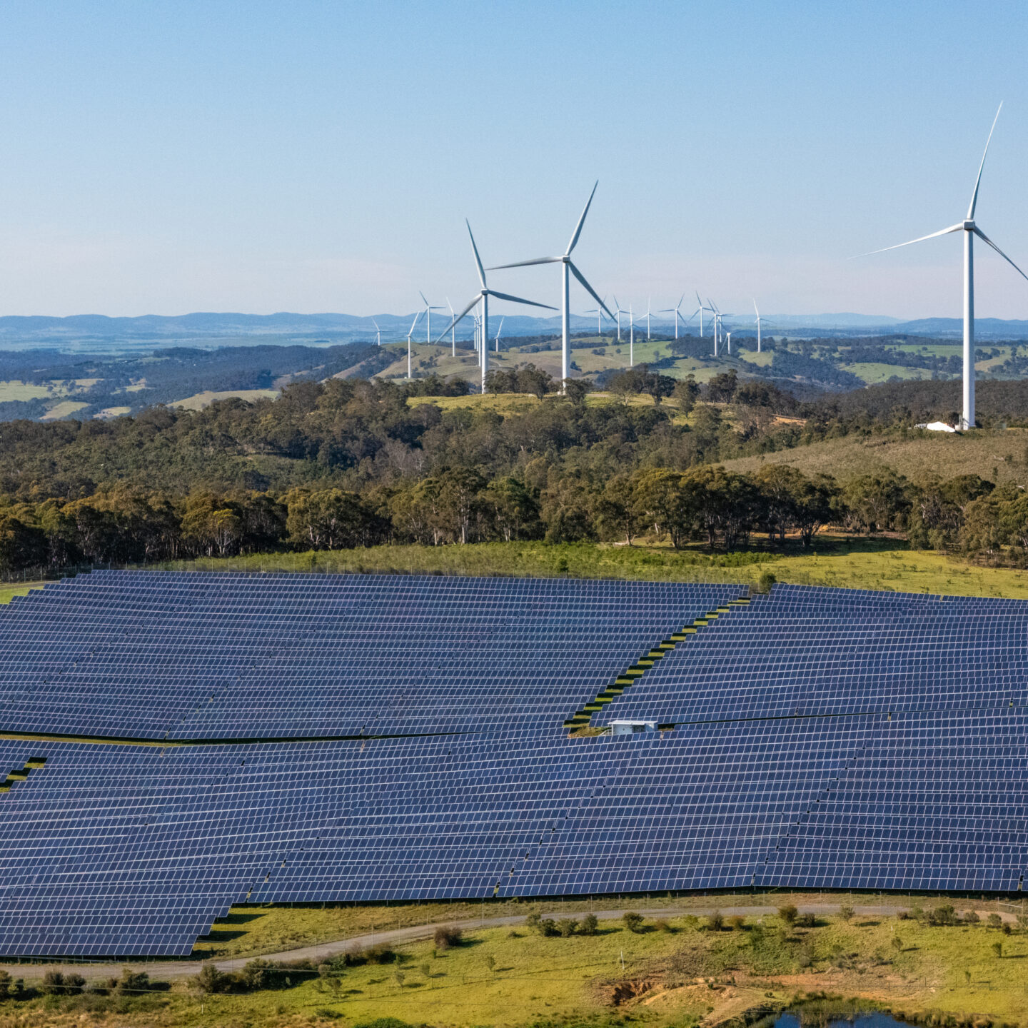 Aerial drone view of a hybrid solar and wind farm showing the large wind turbines in the background for renewable clean energy supply located at Bannister, NSW, Australia on a sunny day