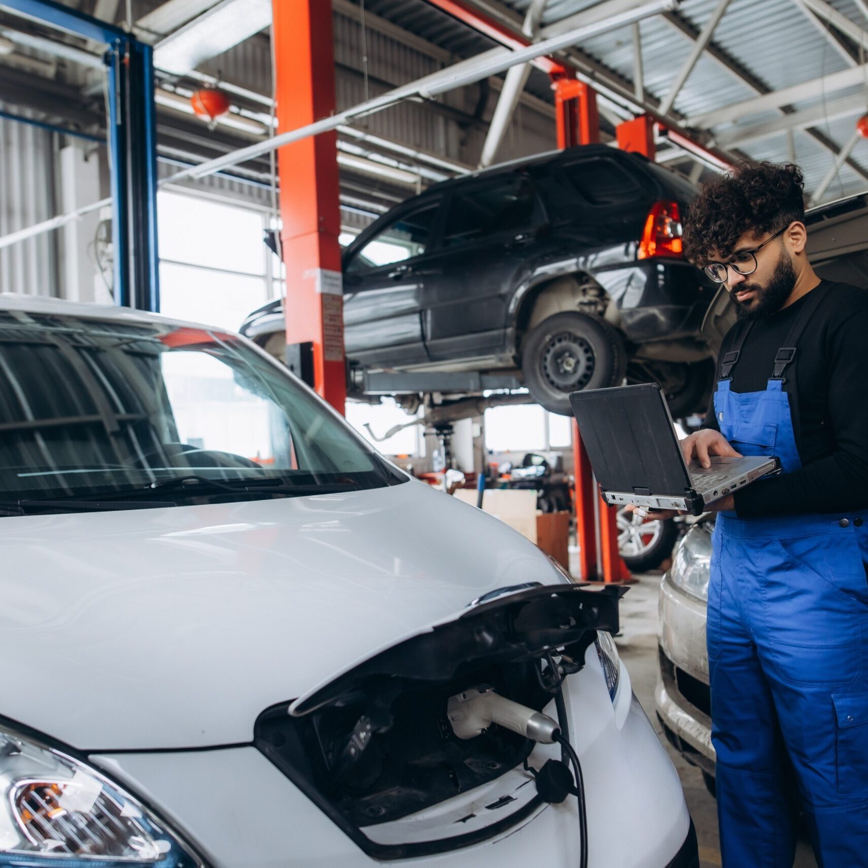 Professional mechanic performing diagnostic check on an electric vehicle with a laptop in a modern auto repair workshop